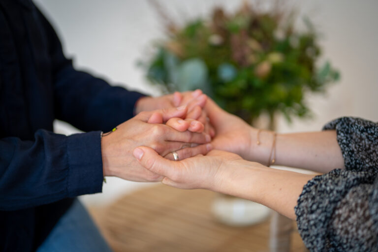 Frau hält Hand einer anderen Frau und spendet ihr damit Trost.